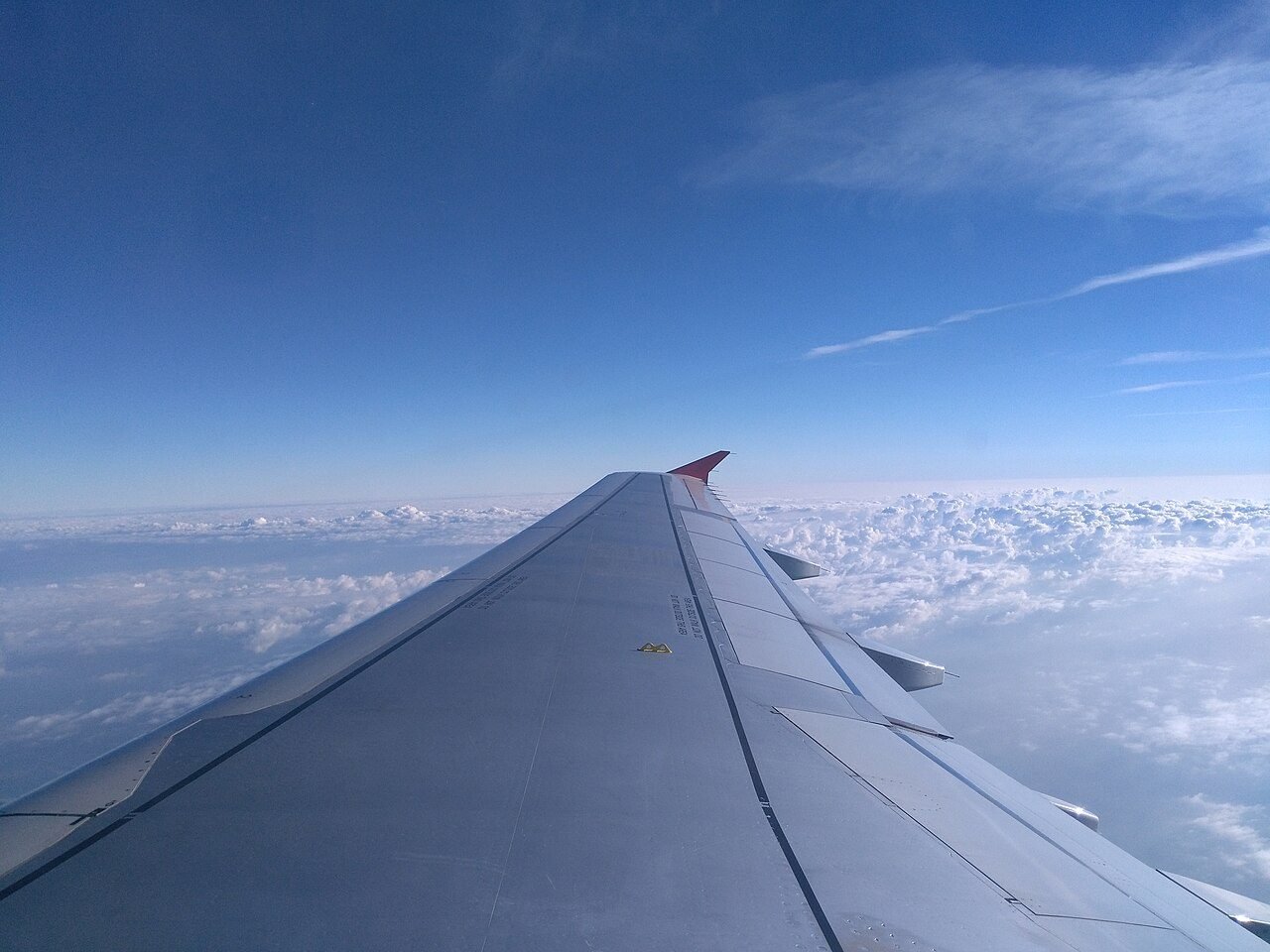 An airplane wing over clouds, illustrating the semi-retired MM2H two-country lifestyle
